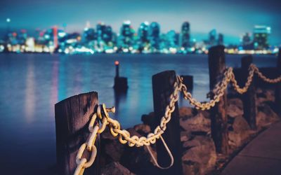 Close-up of fence by river against sky in city at dusk