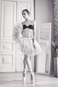 Charming ballerina poses showing her legs in the room in front of the mirror in pointes and tutu