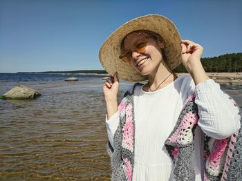 Portrait of a smiling young woman in hat against sky