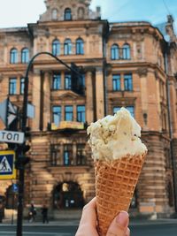 Cropped hand holding ice cream against building in city