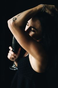 Woman with eyes closed holding red wine while standing against black background