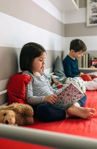 Siblings reading books on bed at home