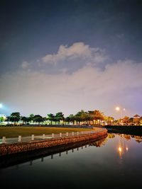 Reflection of illuminated trees and river against sky at night