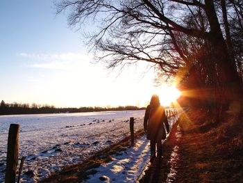 Rear view of man walking on snow covered landscape during sunset