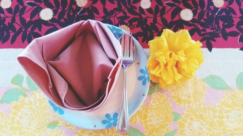 High angle view of yellow flower by napkin and cutlery in plate on table