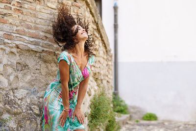 Woman tossing hair while standing against brick wall