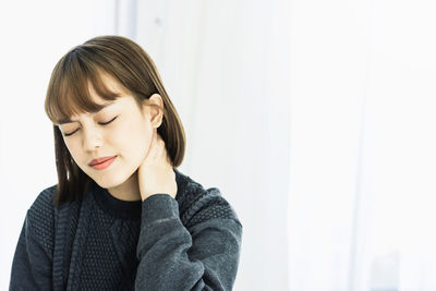 Woman with neck pain sitting against window at home