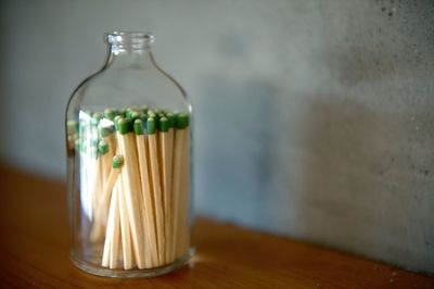 Close-up of matchsticks inside of glass bottle on table against wall