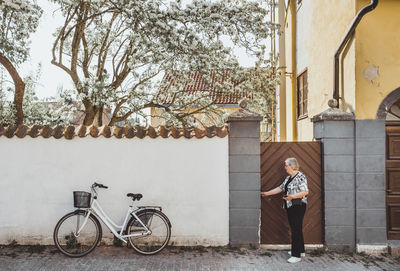 Full length side view of senior female tourist opening gate in city