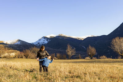 Mother and son standing on field against snowcapped mountains