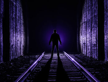 Rear view of silhouette man standing on railroad tracks at night