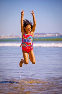 Full length of happy girl jumping in sea against clear sky