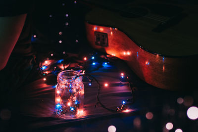 High angle view of illuminated string lights with jar and guitar on bed in darkroom
