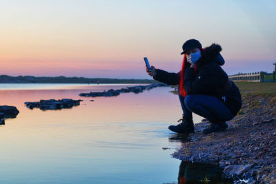 Man sitting on beach against sky during sunset