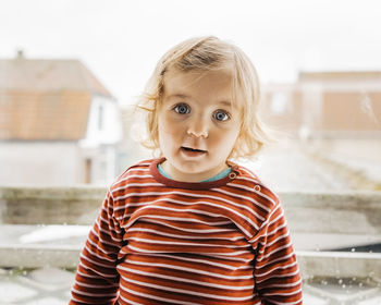 Portrait of cute baby girl standing against window