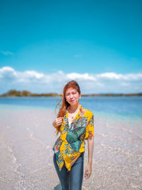 Portrait of smiling young woman standing in sea against sky