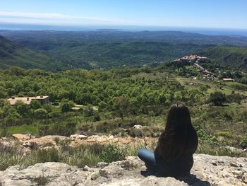 Rear view of woman sitting on landscape against sky