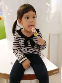 Cute girl eating flavored ice sitting on table at home