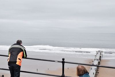 Rear view of man and woman at observation point against beach