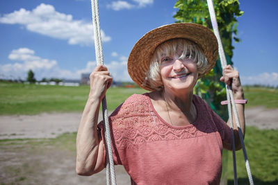 Portrait of smiling woman sitting on swing against sky