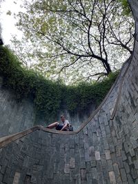 Low angle view of young man sitting on retaining wall