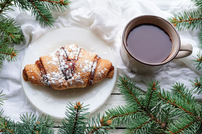 Christmas breakfast. cup of coffee, croissant and tree fir branches on window sill
