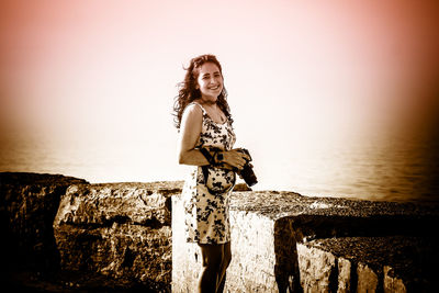 Portrait of young woman standing on rock by sea against sky