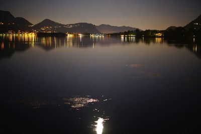 Illuminated city by river against sky at night