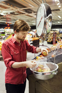 Young man weighing apples at supermarket