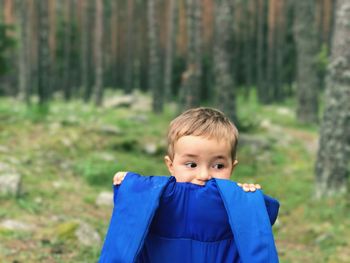 Cute baby boy holding blue life jacket against trees at forest