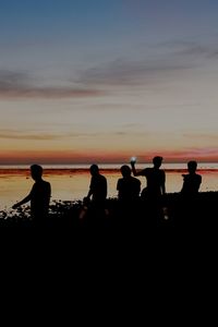 Silhouette people on beach against sky during sunset