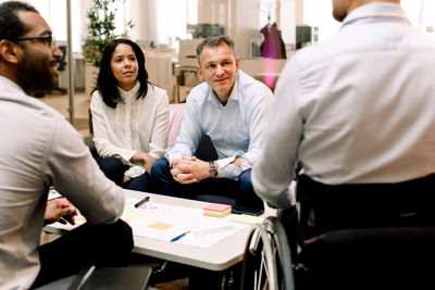 Business colleagues looking at disabled sales manager during meeting in office