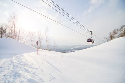 Overhead cable car over snow covered land against sky