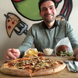 Happy man sitting in front of pizza and burger at restaurant