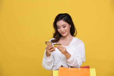 Young woman using mobile phone against yellow background