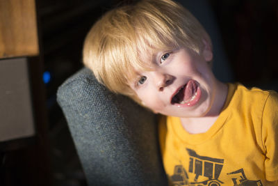 Portrait of boy sticking out tongue while leaning on sofa at home