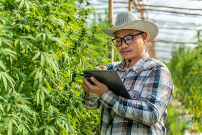 Young woman using mobile phone while standing against plants