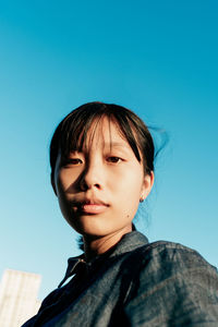 Portrait of young woman standing against clear blue sky