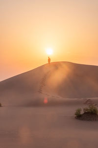 Solo traveler walking down dune against sunrise.