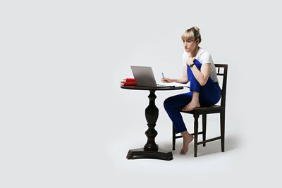 Portrait of woman using laptop while sitting against white background