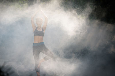 Teenage girl practicing tree pose in forest during foggy weather