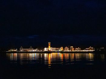 Illuminated buildings by sea against sky at night