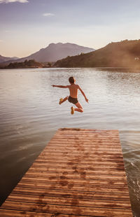 Rear view of boy jumping in lake during sunset