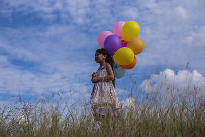 Low angle view of cute girl holding balloons while standing on land against sky