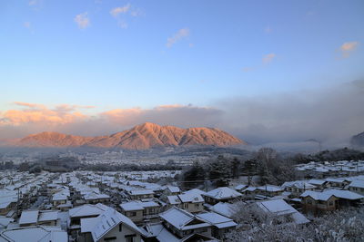 Snow covered houses by mountain against sky