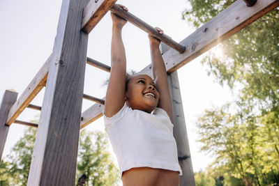 Low angle view of smiling girl hanging while doing monkey bars at summer camp