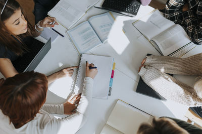 High angle view of students studying together at desk in classroom