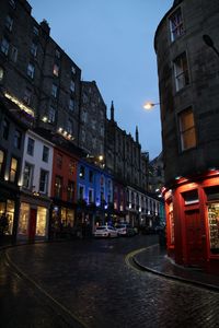 Illuminated street amidst buildings in city at dusk