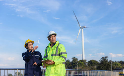 Female engineer holding model wind turbine against sky