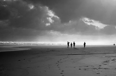 Silhouette people at beach against cloudy sky